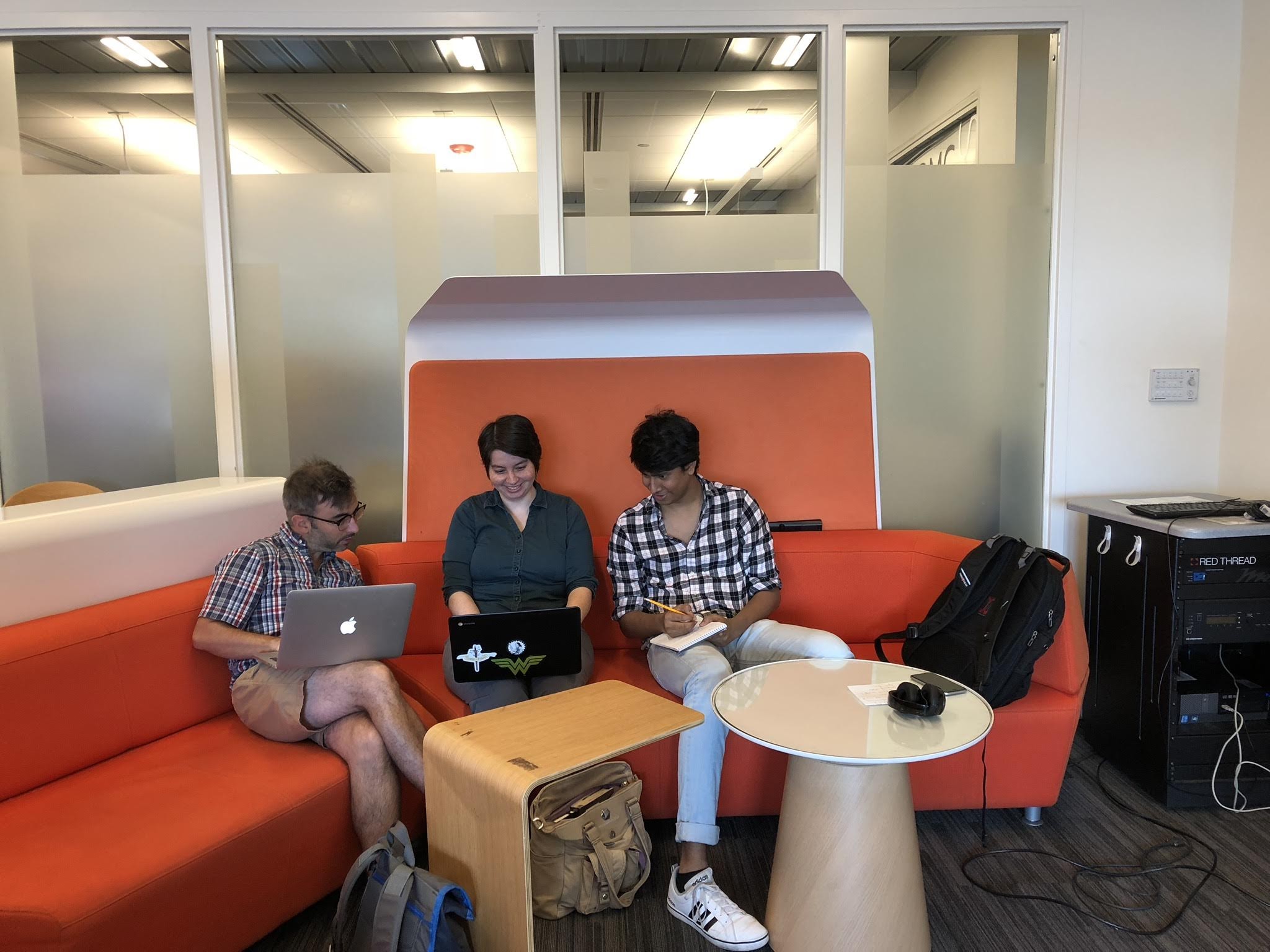 Two people peer at a third person's laptop.